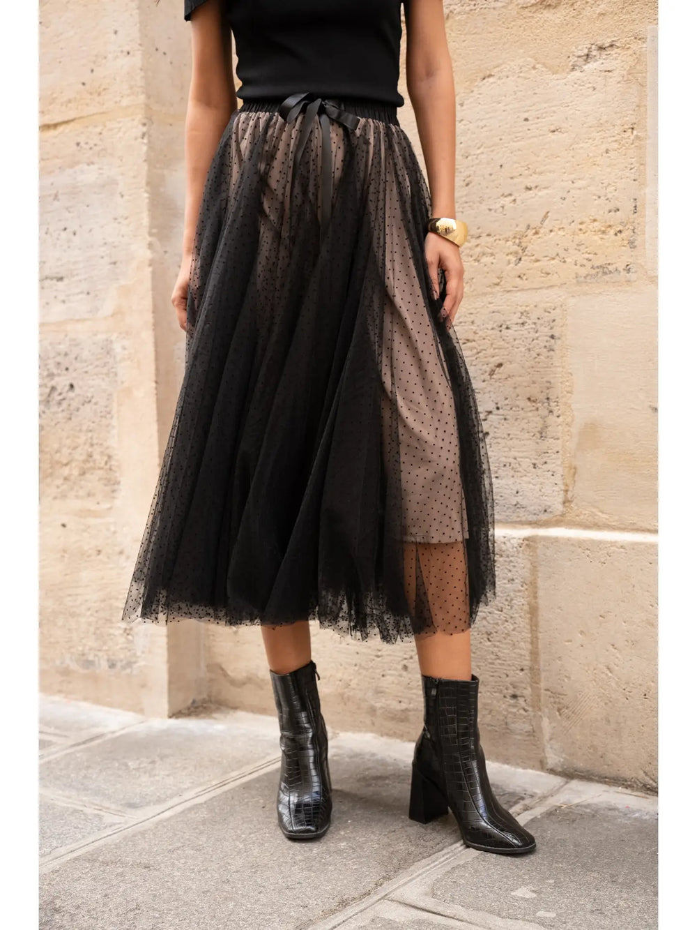 Person wearing a black tulle skirt and black boots against a stone wall.