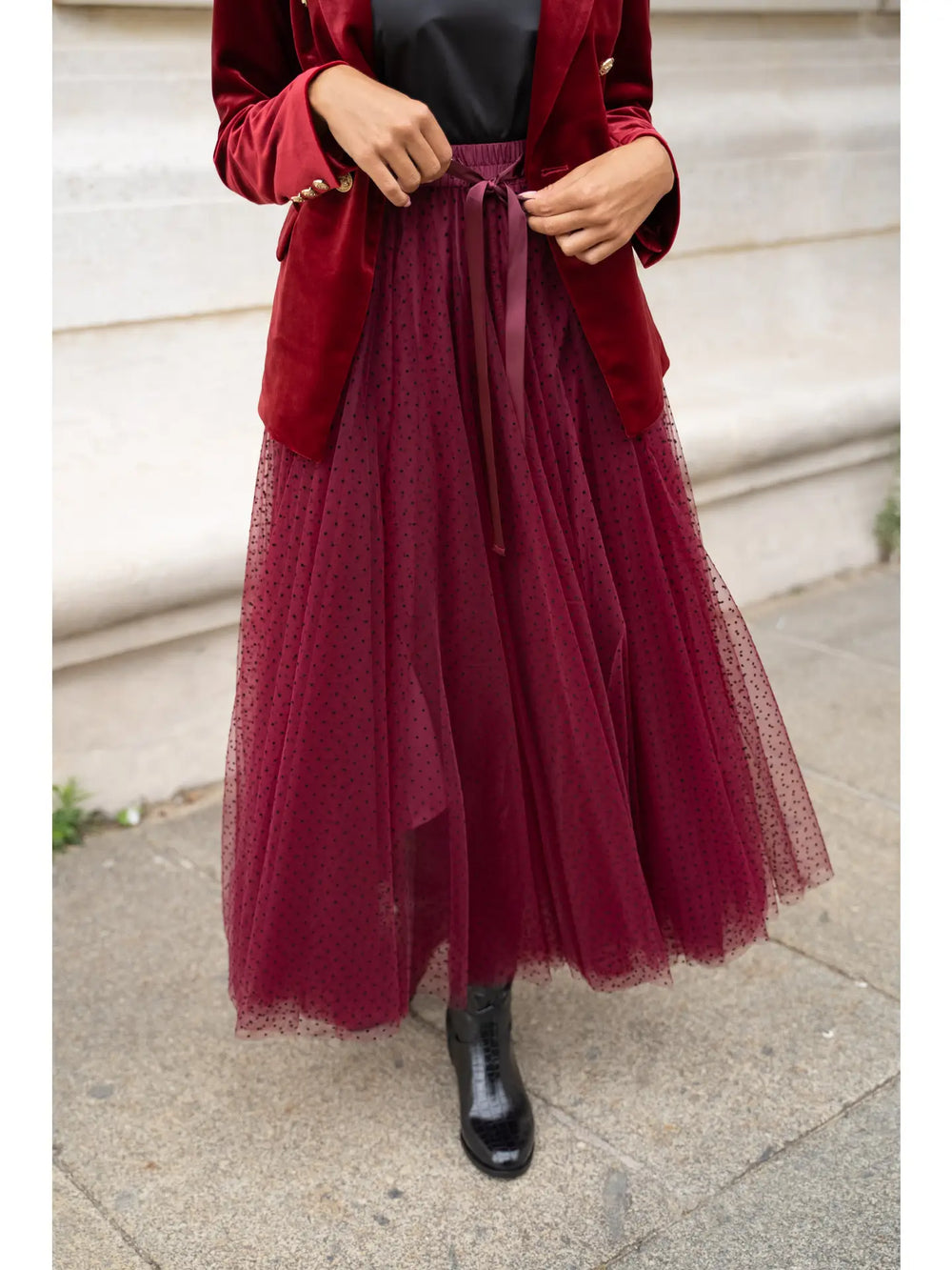 Person wearing a red coat and burgundy tulle skirt on a sidewalk.