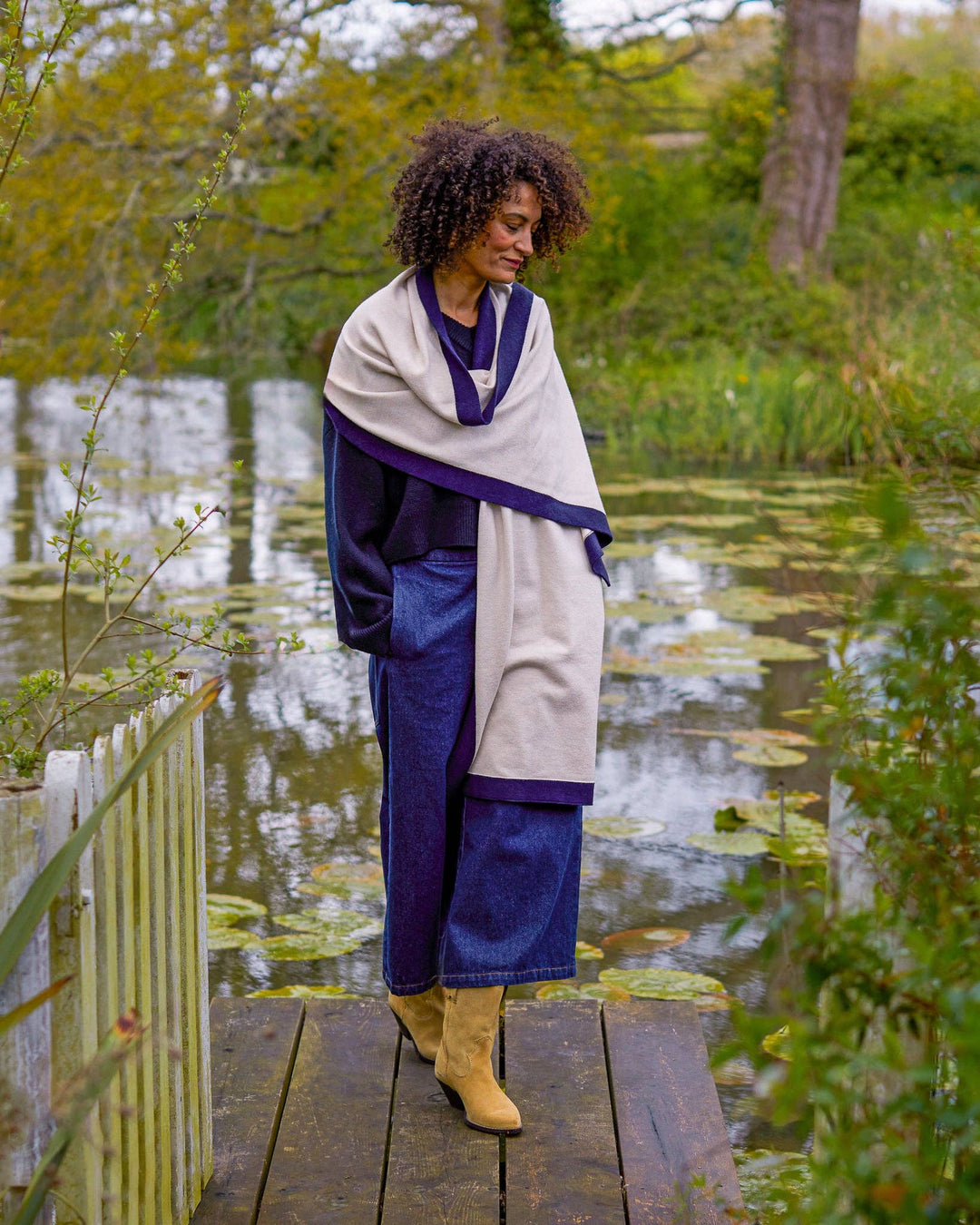 Woman standing on a wooden bridge over a pond, wearing a blue and white outfit.