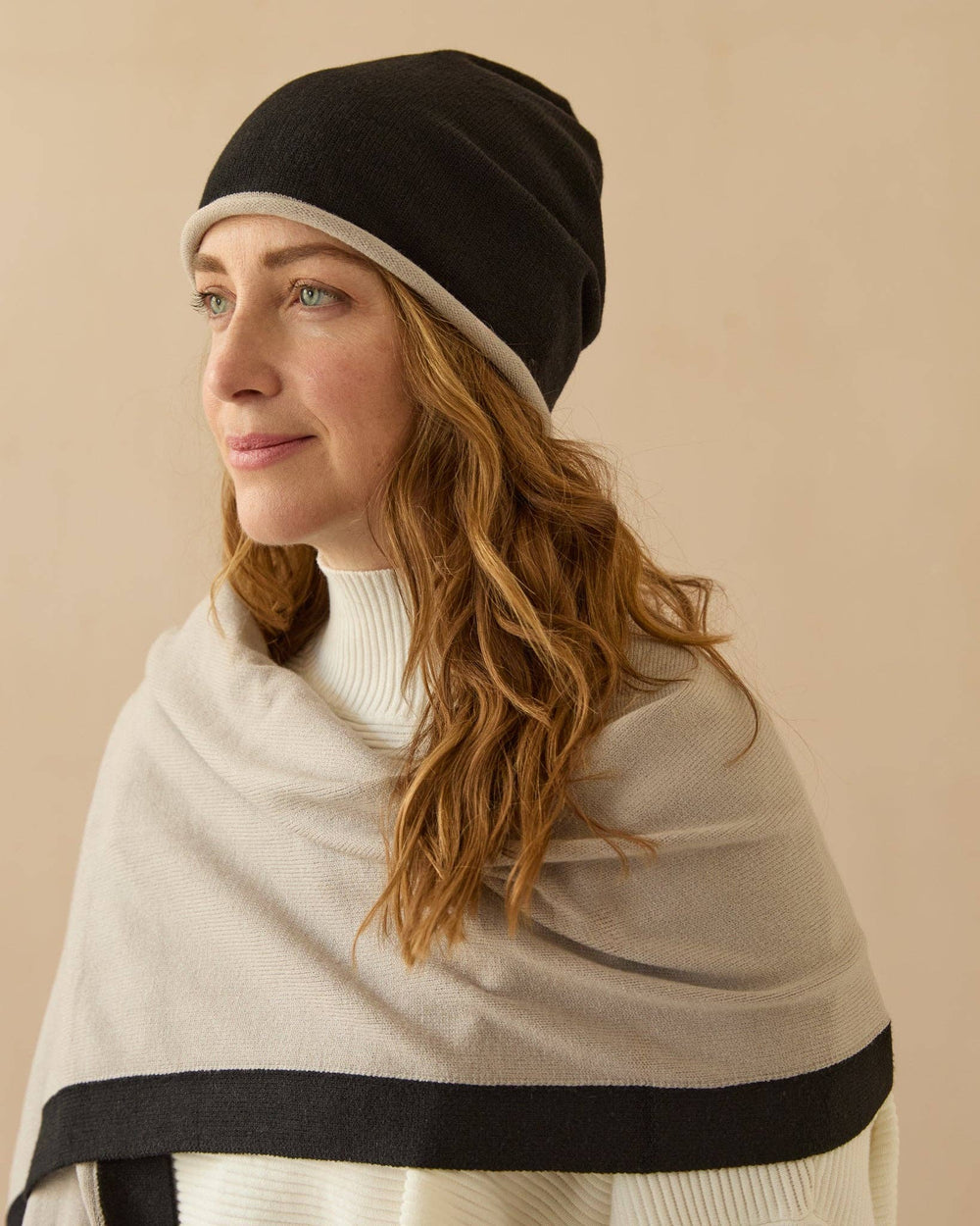 Woman wearing a black beanie and beige shawl against a beige background
