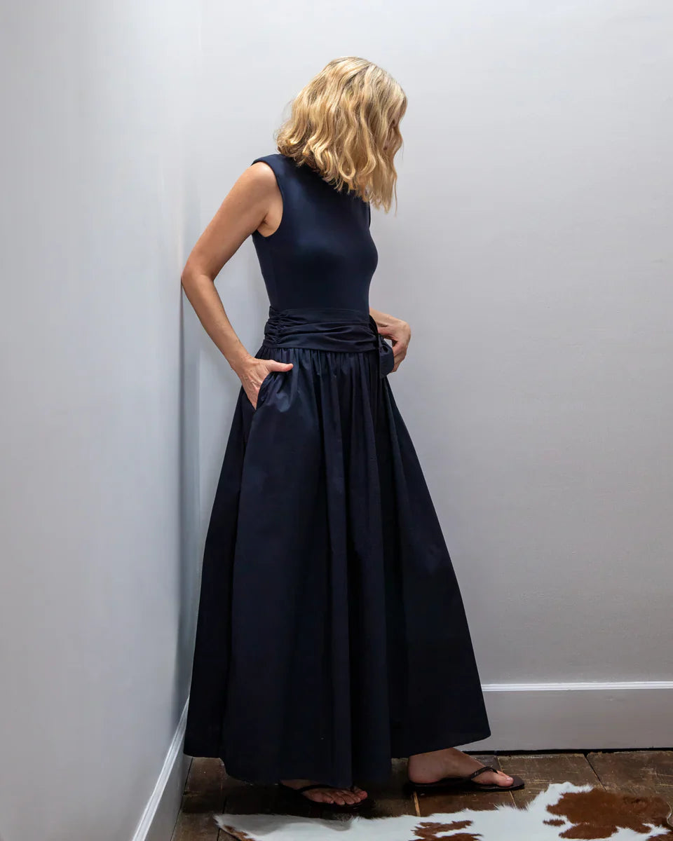 Woman wearing a long black dress against a plain white wall.