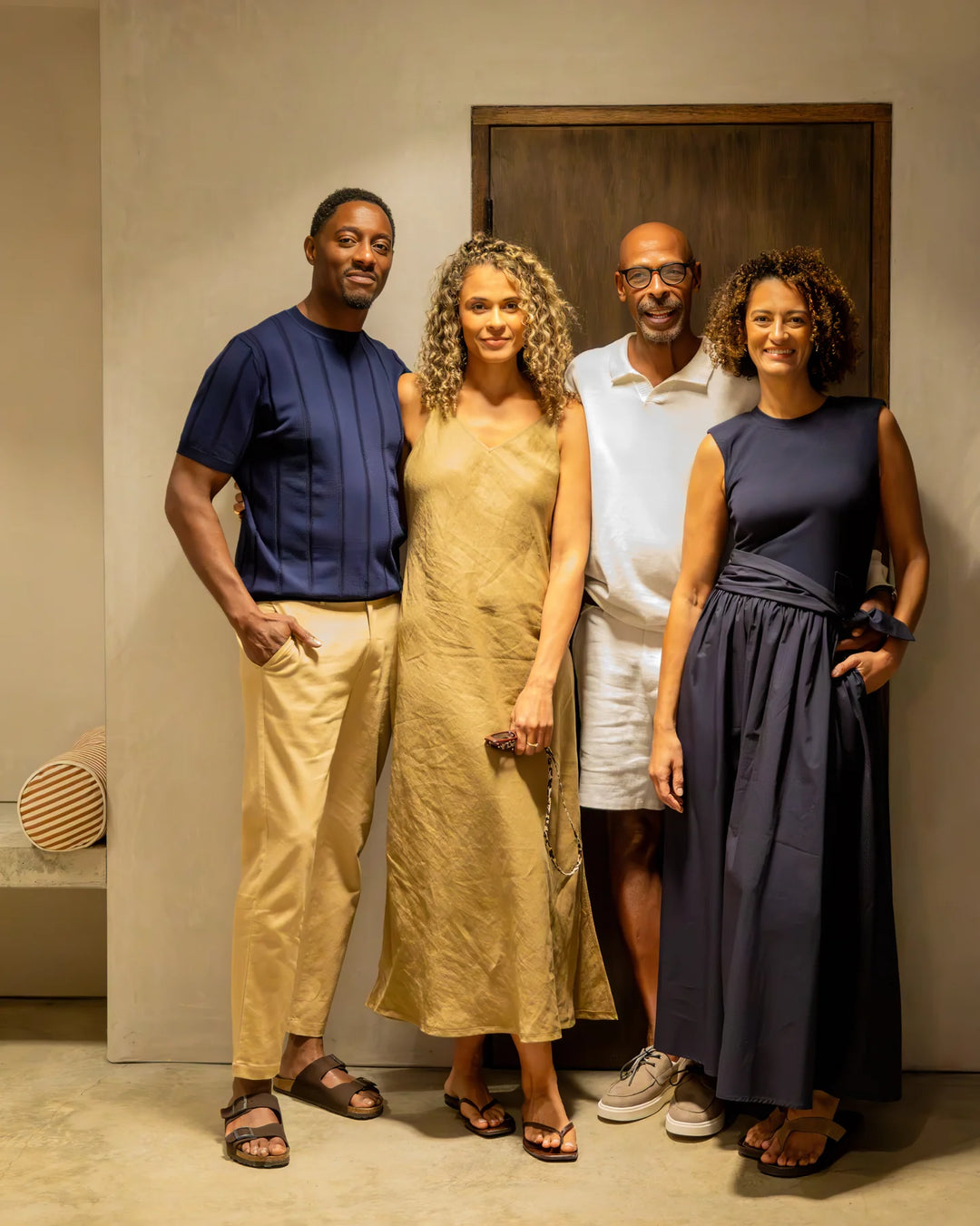 Four people posing together in a room with a wooden door.