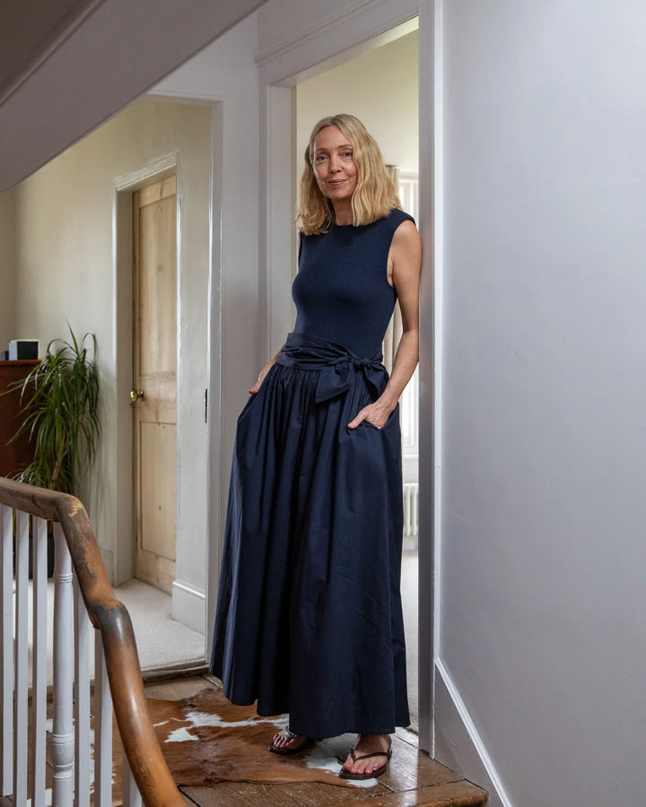 Woman in a navy blue dress standing in a doorway of a home.