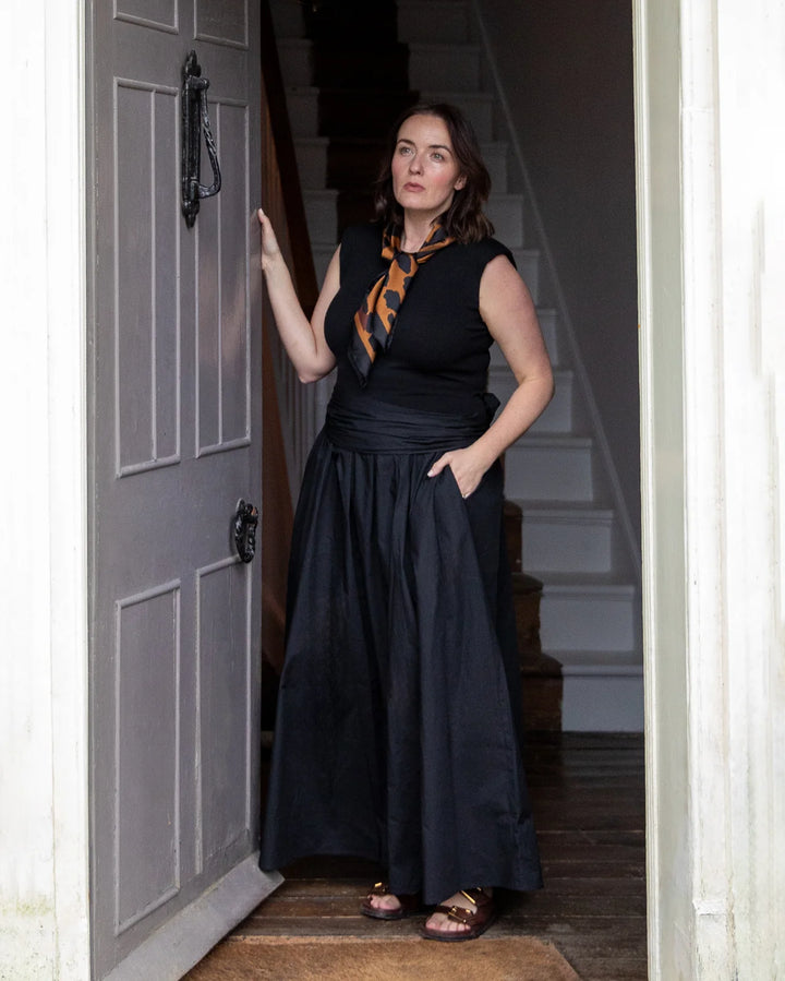 Woman in a black dress standing in a doorway with a staircase in the background