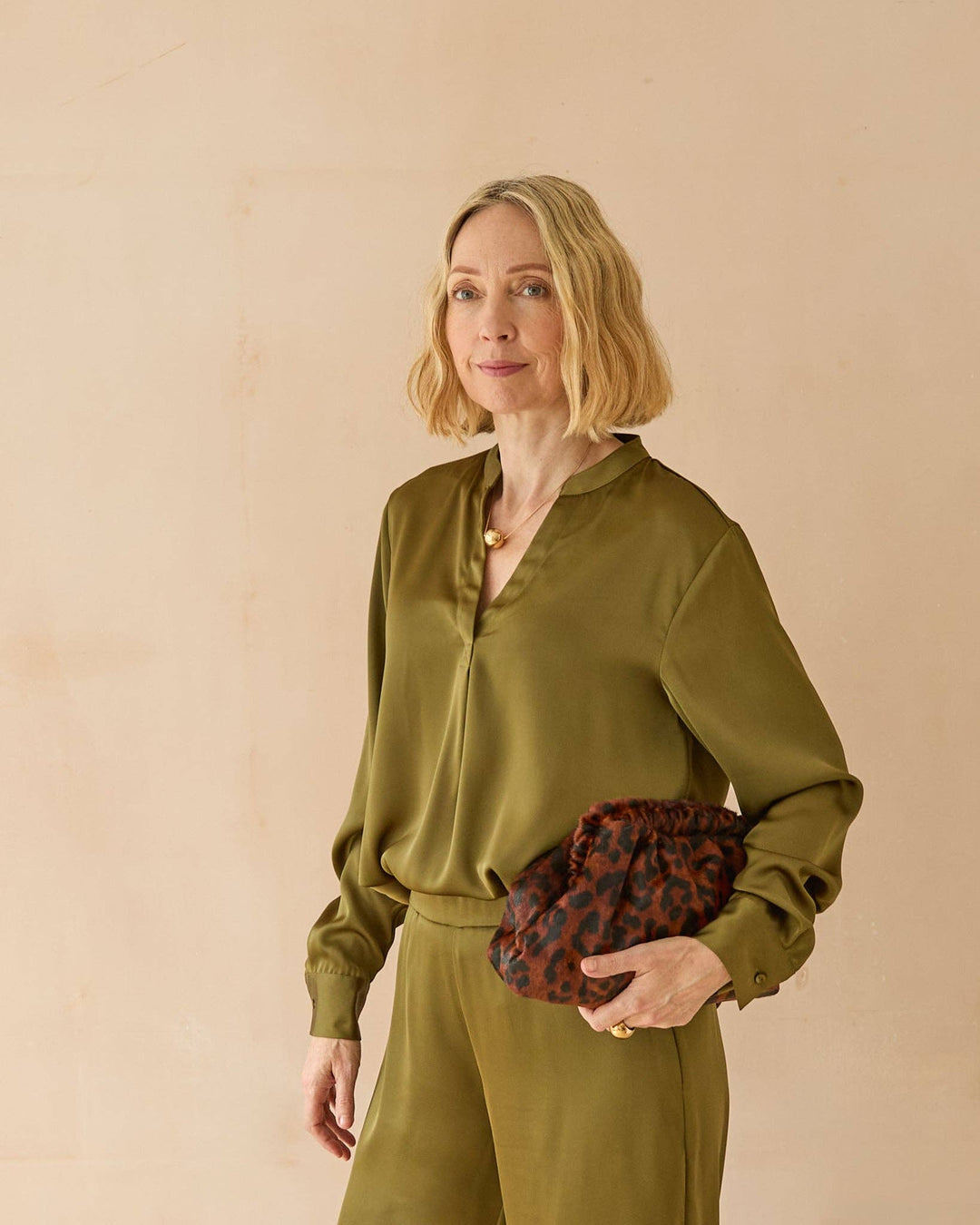 Woman in a green outfit holding a leopard print clutch against a beige background