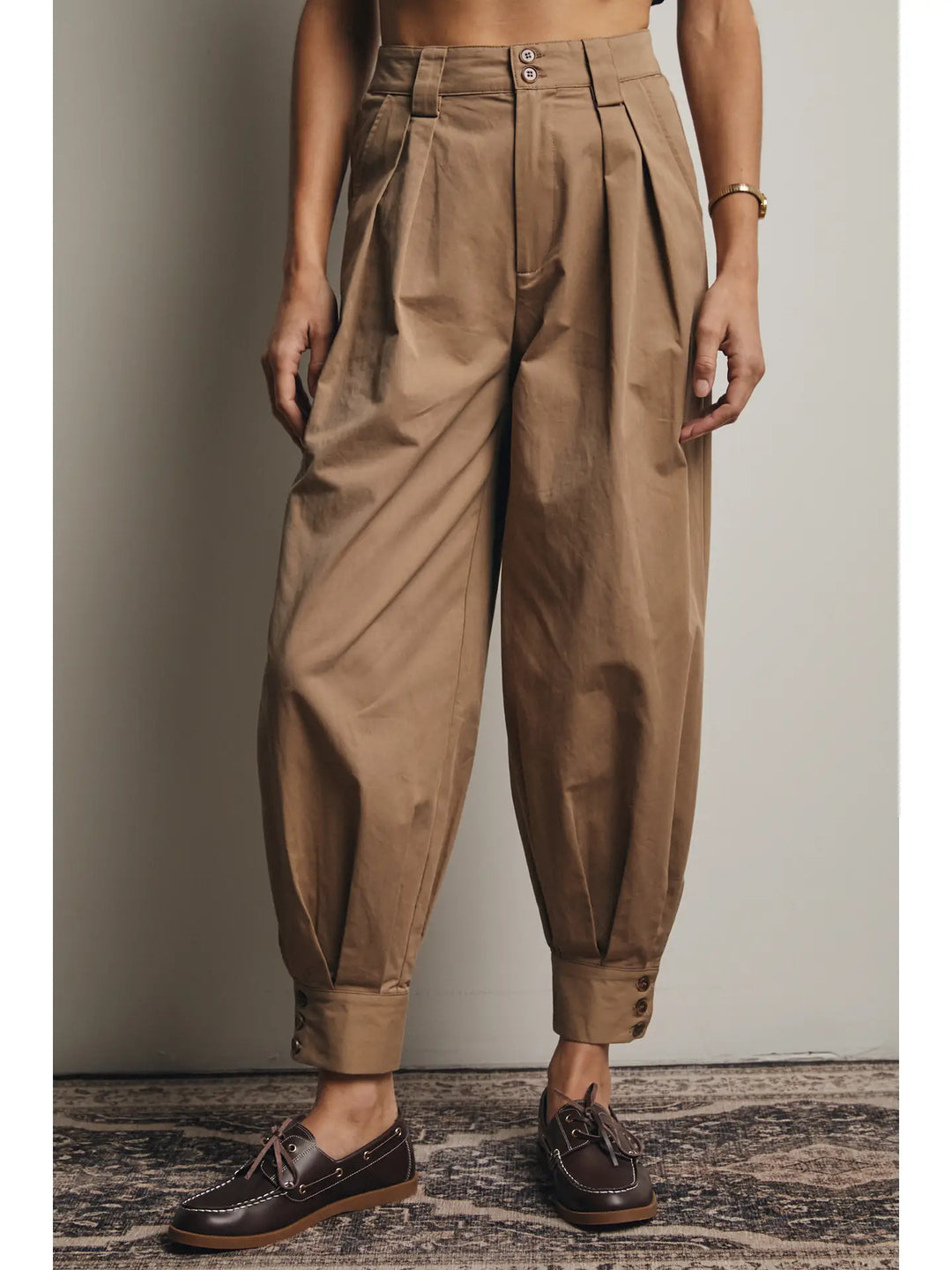 Person wearing brown pleated pants against a neutral background