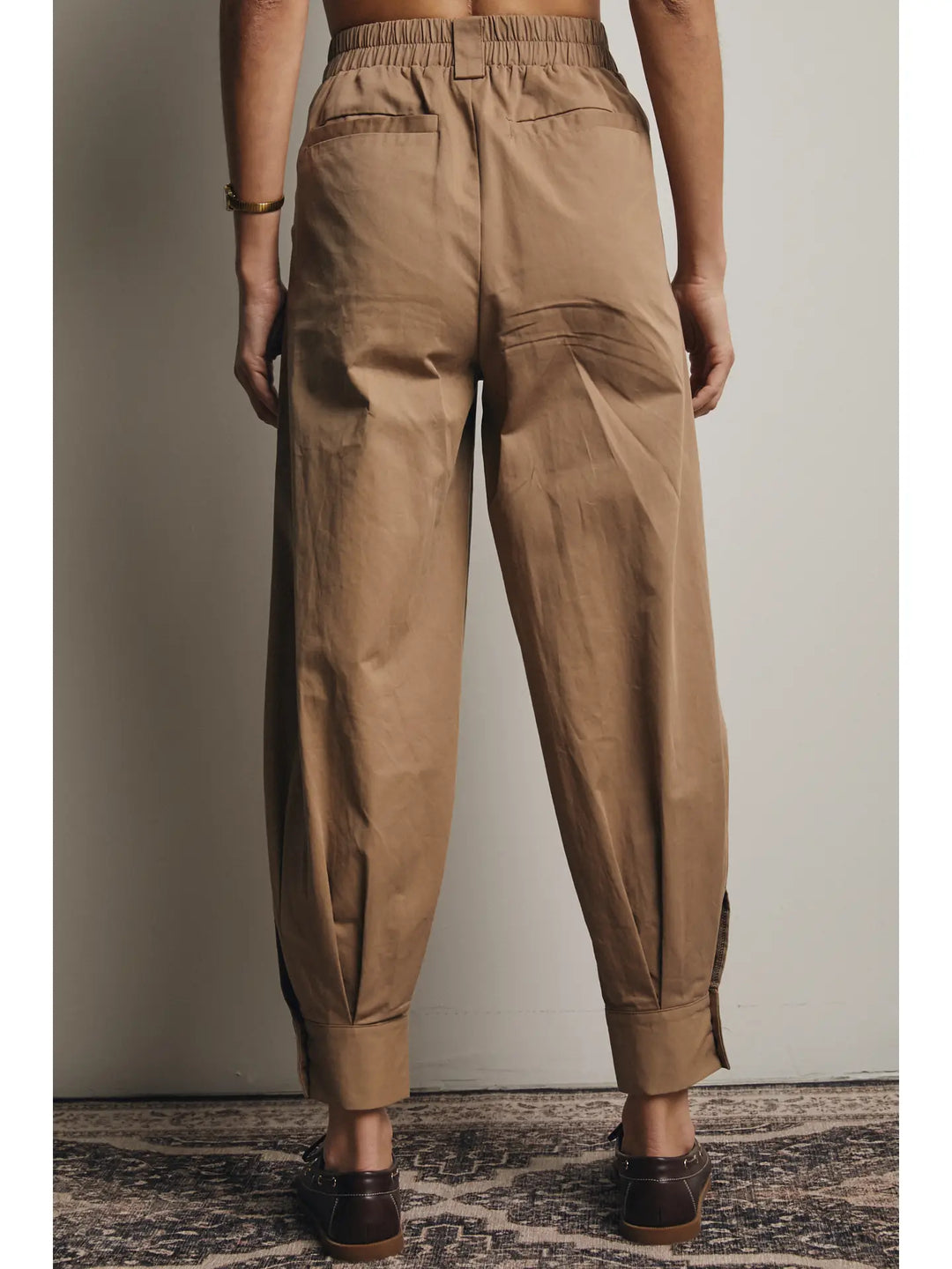 Person wearing brown pants standing against a plain background