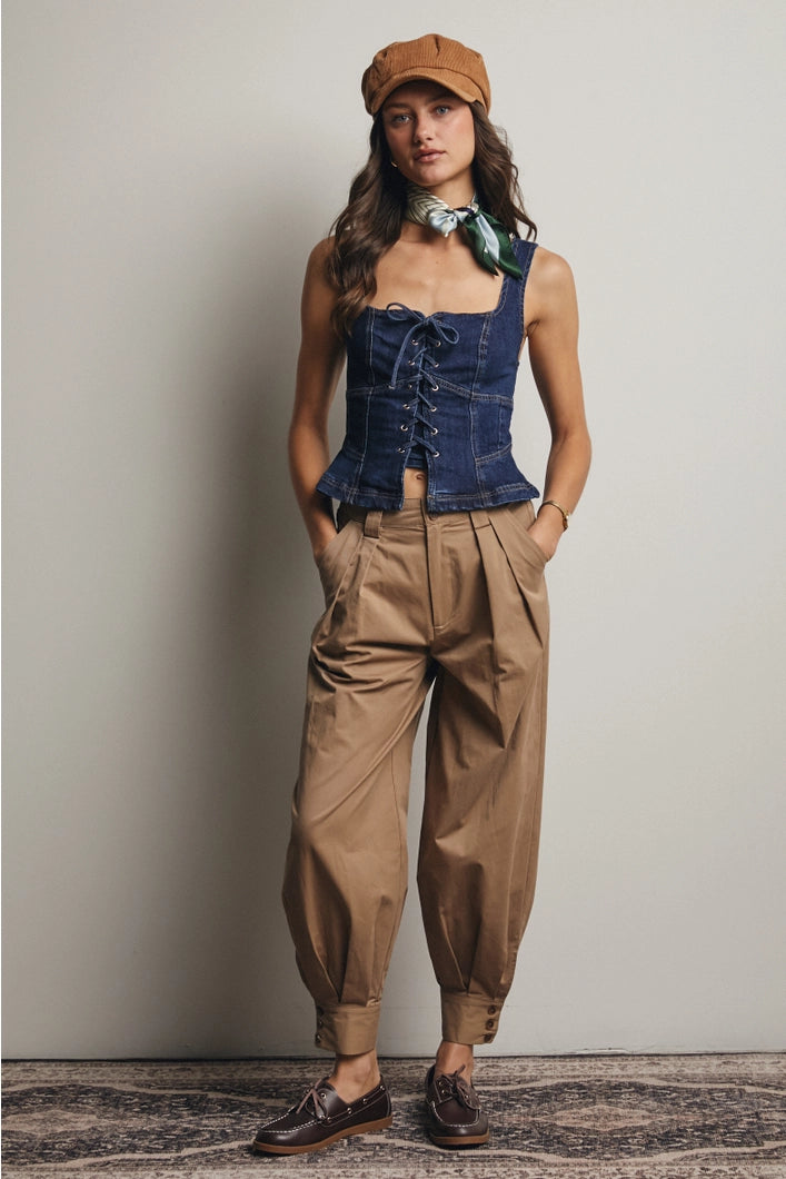 Woman wearing a denim corset top and beige pants with a brown cap against a plain background