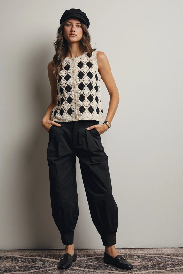 Woman wearing a sleeveless patterned top and black pants against a plain background