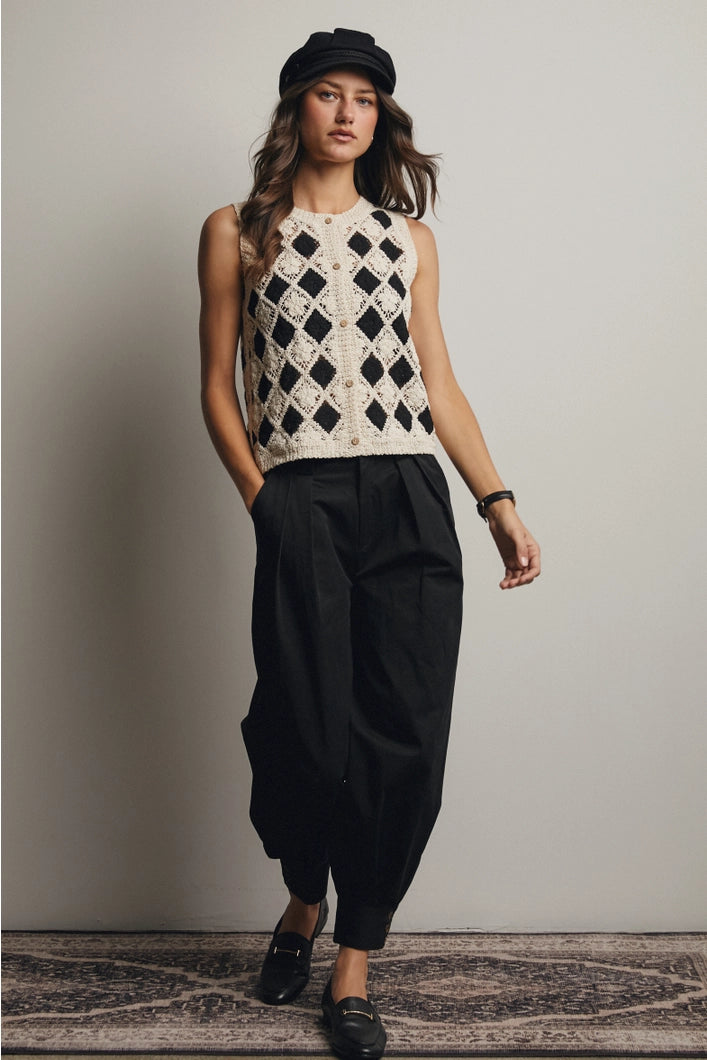 Woman wearing a sleeveless black and white patterned top with black pants against a plain background