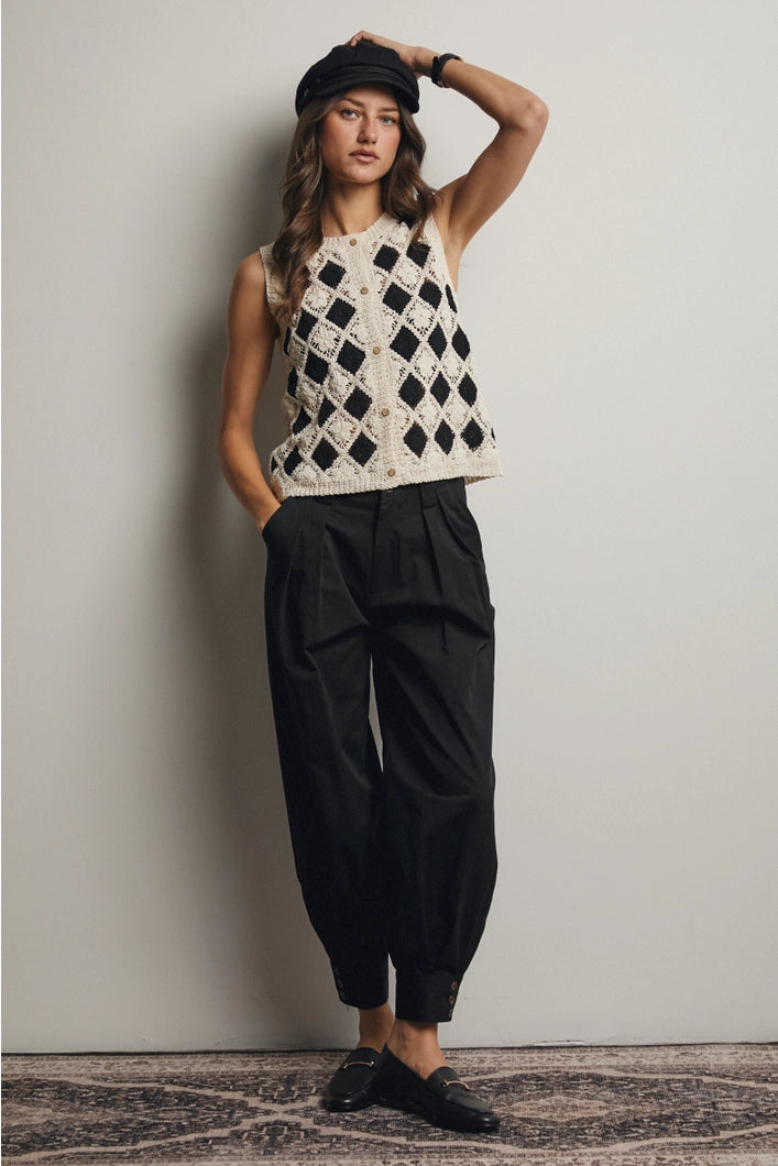 Woman wearing a black and white patterned sleeveless top and black pants against a plain background