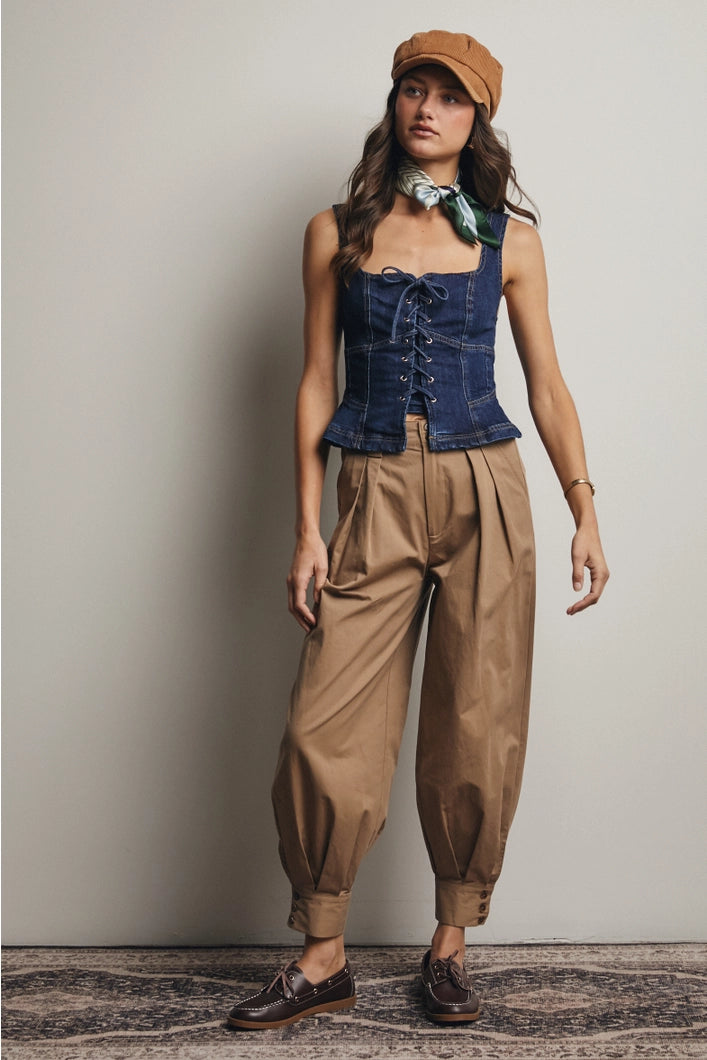 Woman wearing a denim corset top and brown pants with a beige cap against a neutral background
