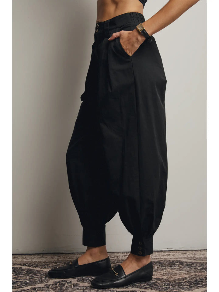 Person wearing black harem pants and black loafers on a neutral background