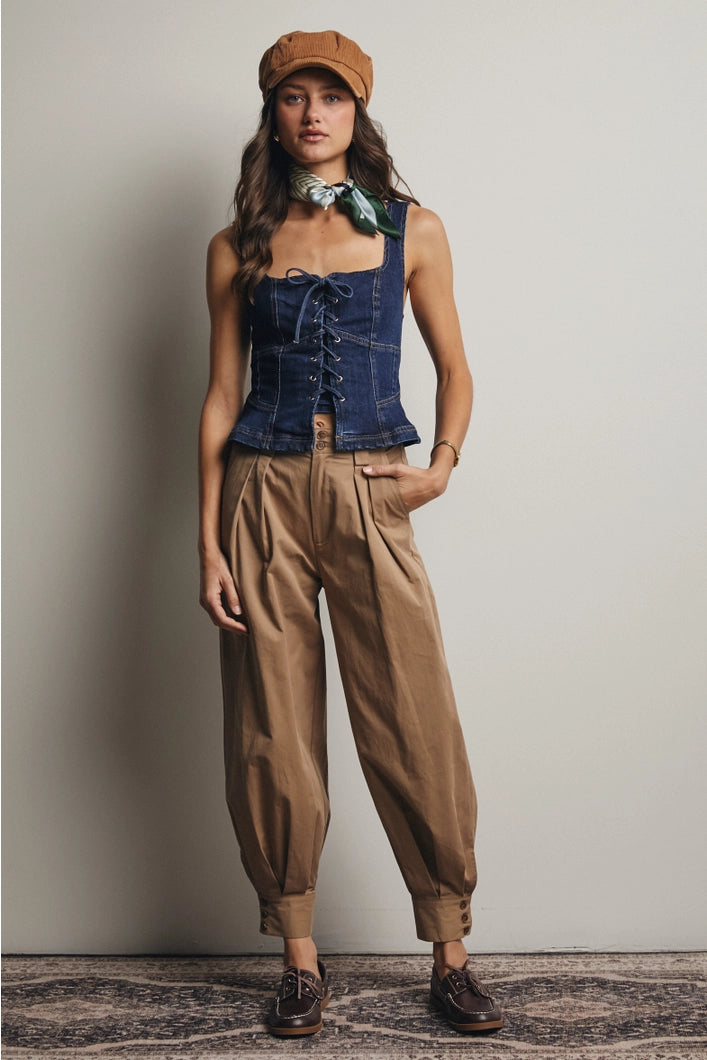 Woman wearing a denim corset top and brown pants against a plain background
