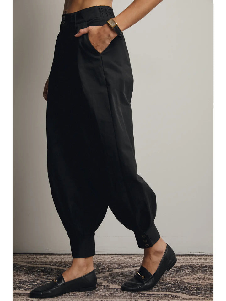Person wearing black harem pants and black loafers on a neutral background