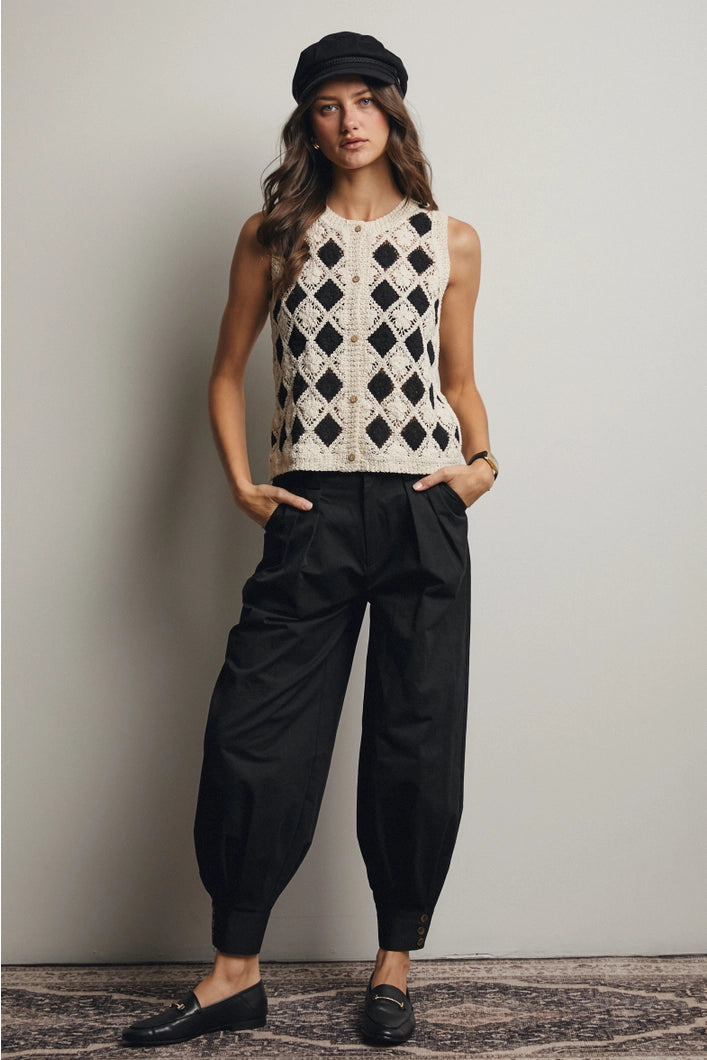 Woman wearing a sleeveless patterned top and black pants against a plain background