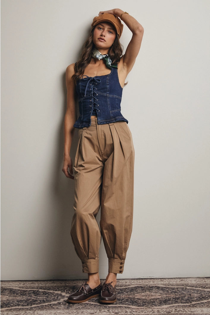 Woman wearing a denim vest, beige pants, and a brown cap against a plain background