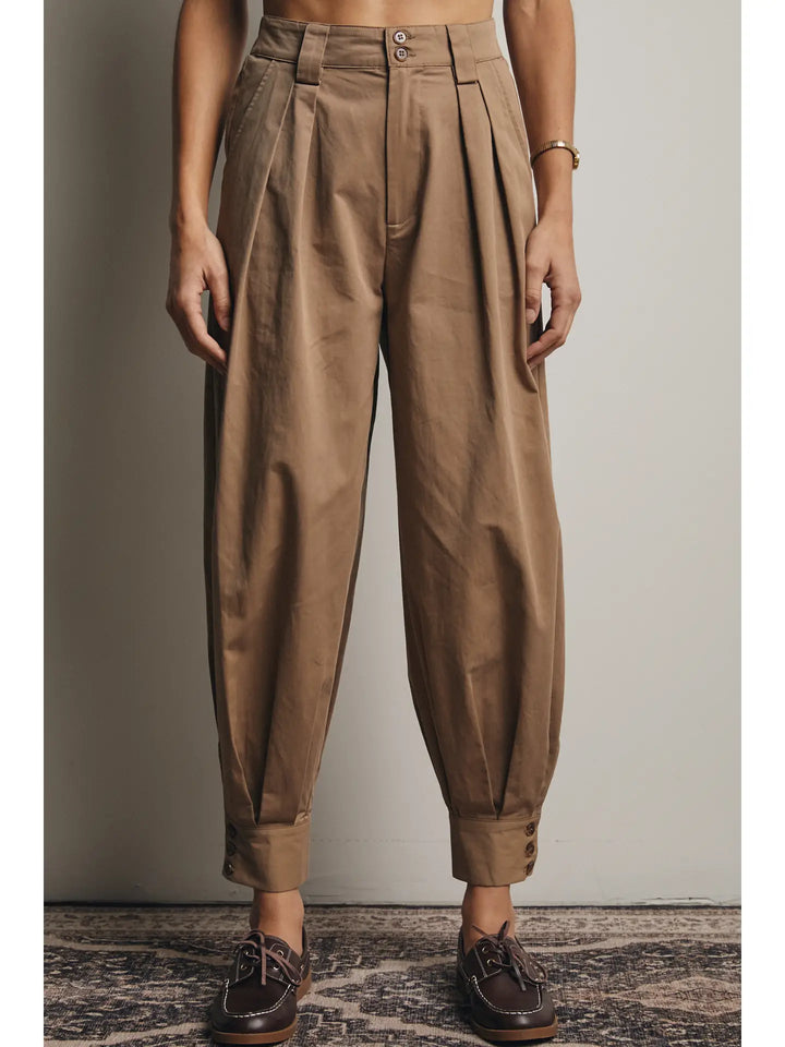 Brown pleated pants worn by a person against a neutral background