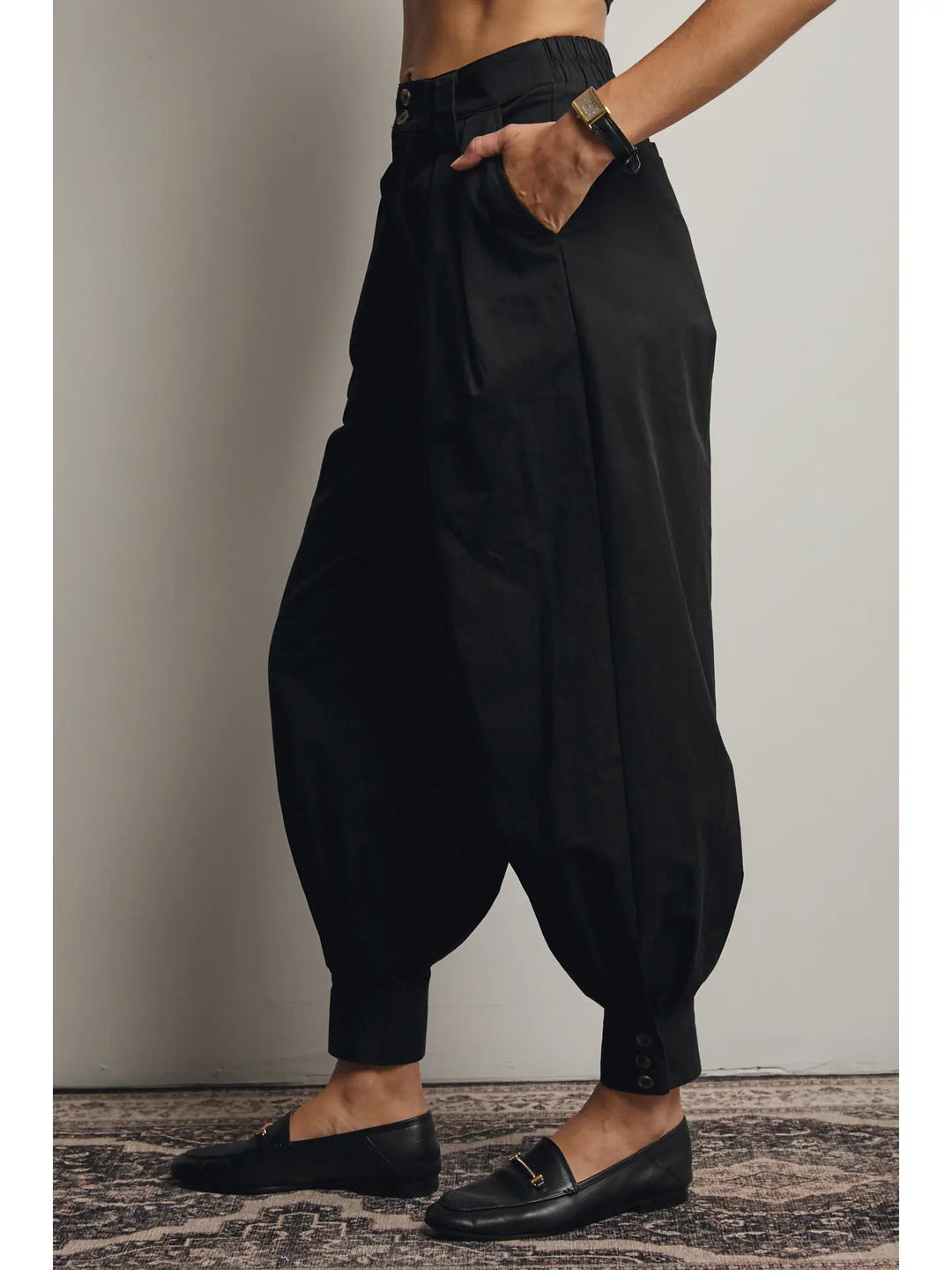 Person wearing black harem pants and black loafers on a neutral background