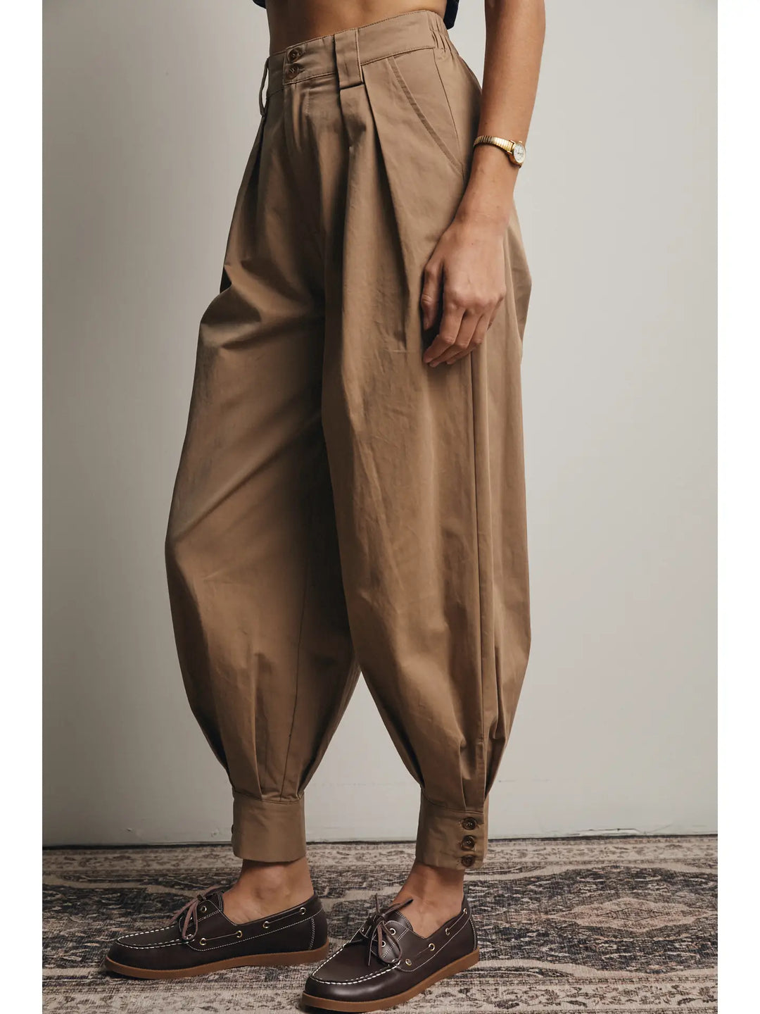 Person wearing brown high-waisted pants with a neutral background