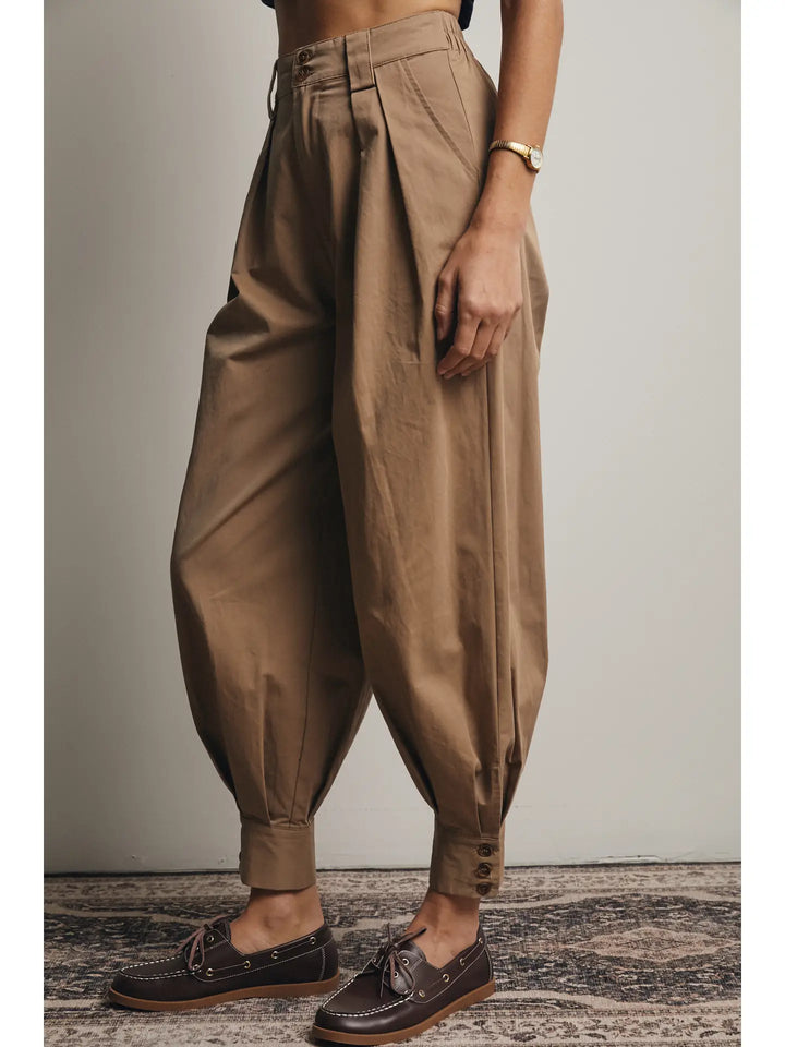 Person wearing brown high-waisted pants with a neutral background