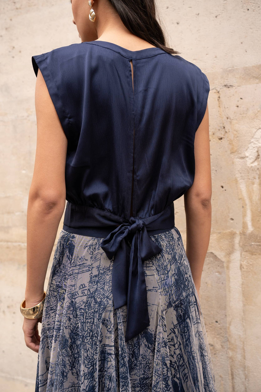 Navy blue top with a tie detail worn by a person against a beige wall.