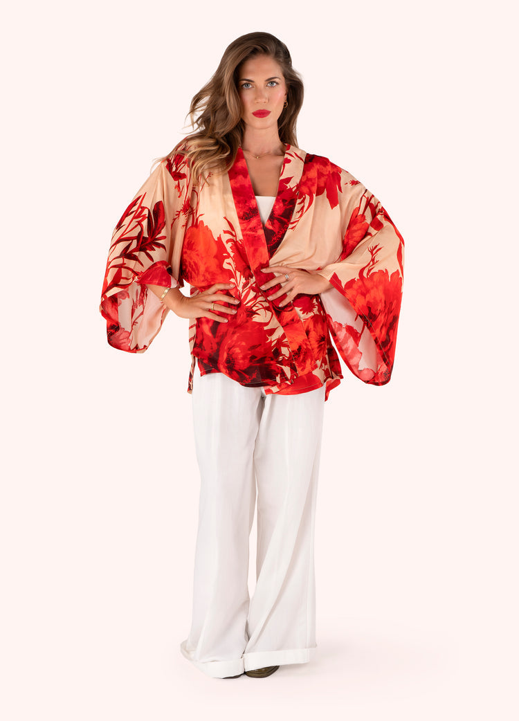 Woman wearing a red and beige patterned kimono-style top with white pants on a white background