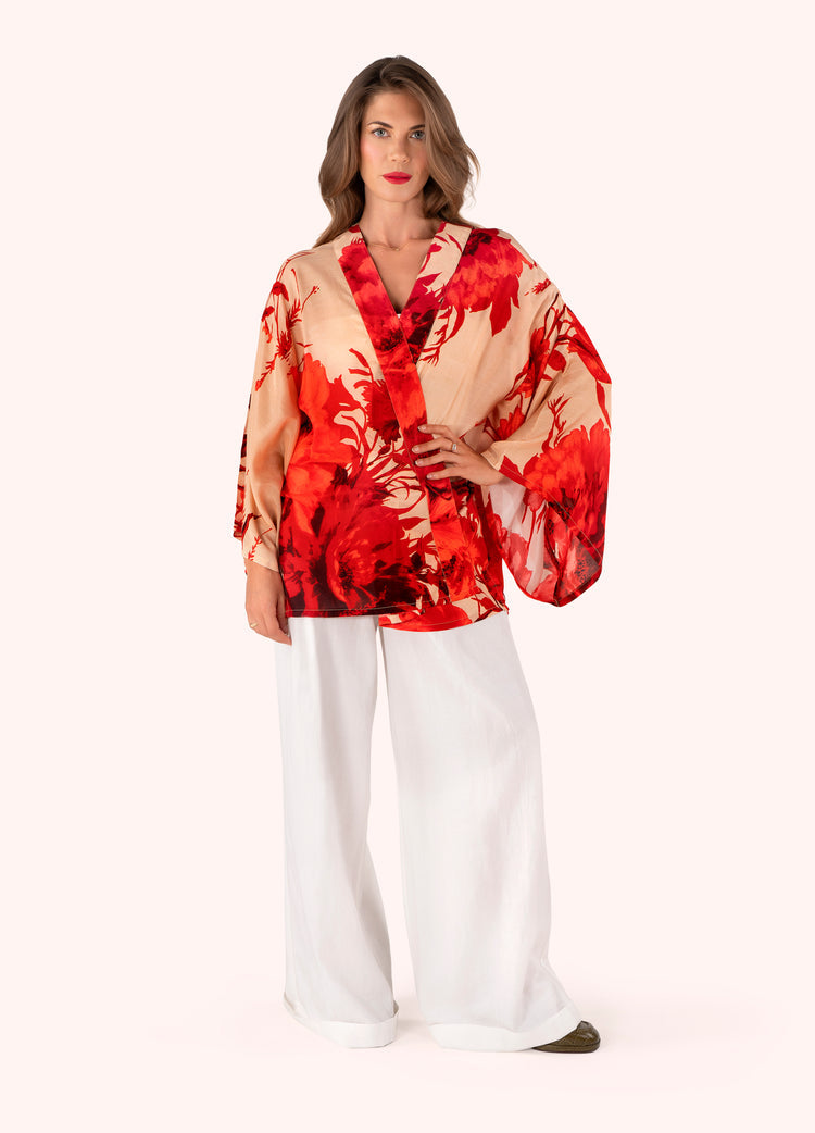 Woman wearing a red and beige patterned blouse with white pants on a white background