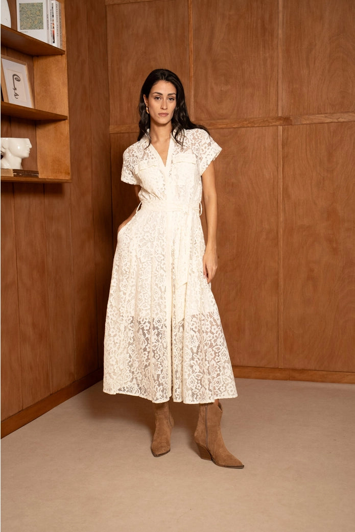 Woman wearing a white lace dress and brown boots in a room with wooden walls.