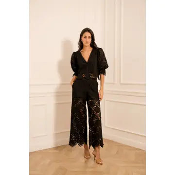 Woman wearing a black outfit with lace details in a room with white walls and wooden floor.