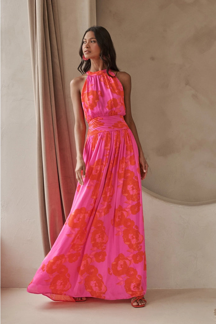 Woman wearing a pink and orange floral dress against a beige wall.