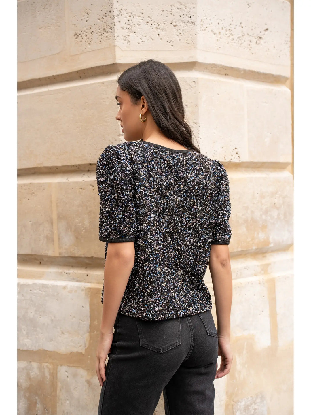 Woman wearing a black and white patterned top against a stone wall.