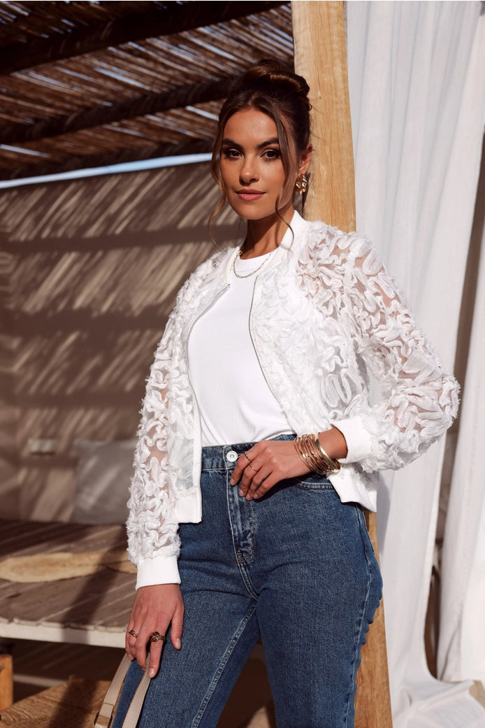Woman wearing a white lace top and blue jeans standing outdoors.