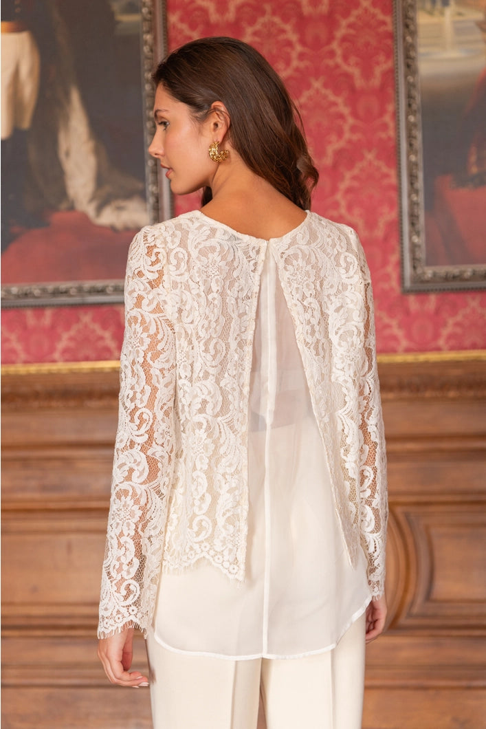 Woman wearing a white lace blouse in an elegant room with red walls and framed pictures.