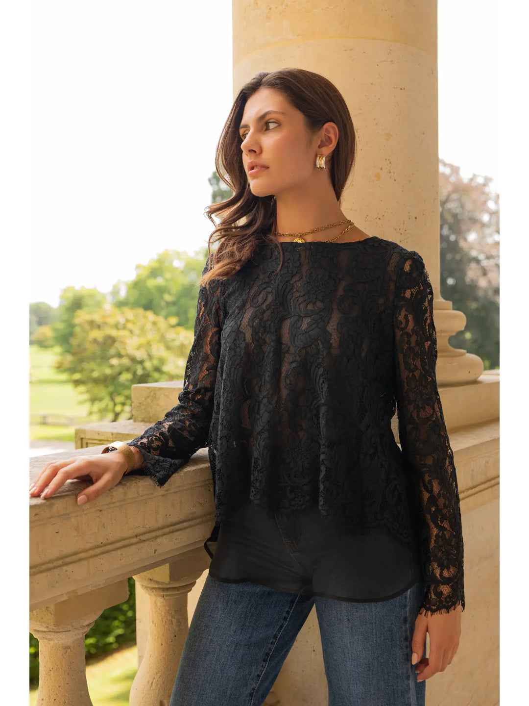 Woman wearing a black lace top and jeans standing outdoors.