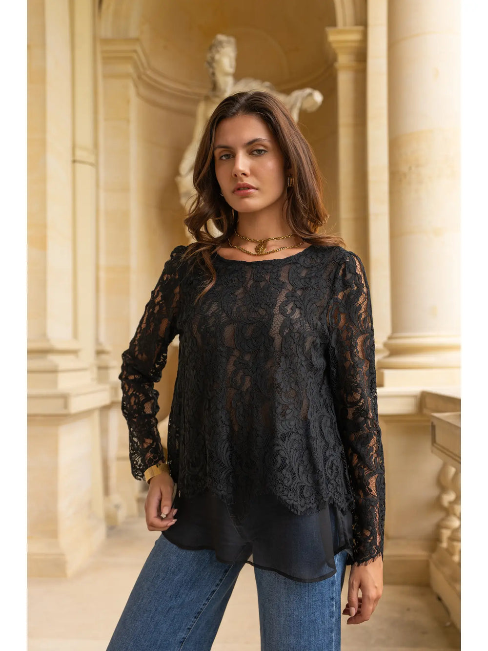 Woman wearing a black lace top and blue jeans in an elegant interior setting