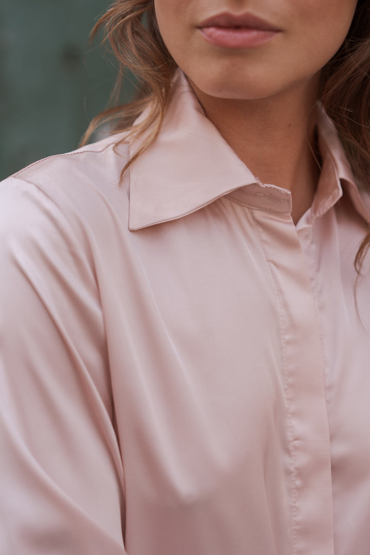 Close-up of a woman wearing a light blush pink satin button-up shirt with a pointed collar.