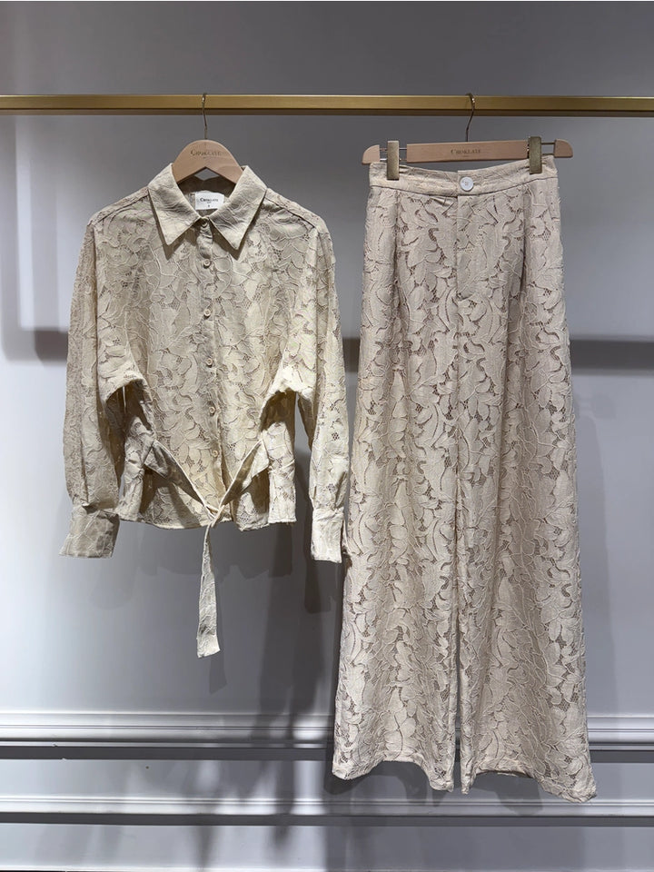 Light-colored lace shirt and skirt set on hangers against a gray background