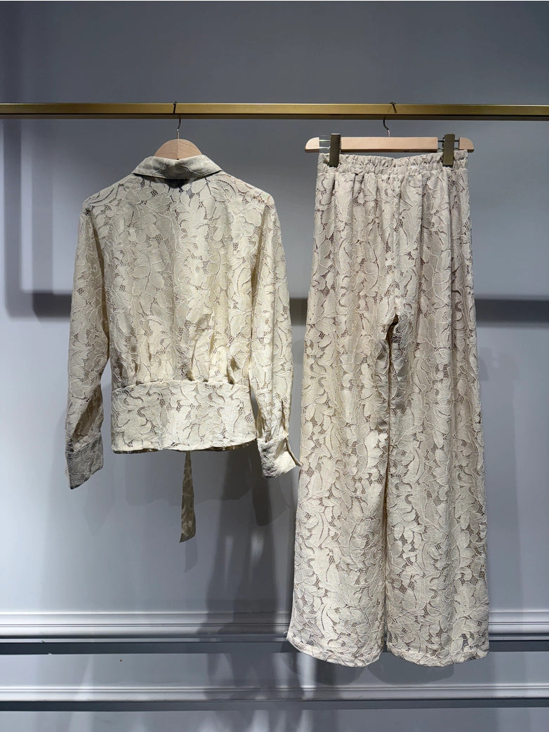 Light-colored lace outfit with jacket and pants on hangers against a neutral background