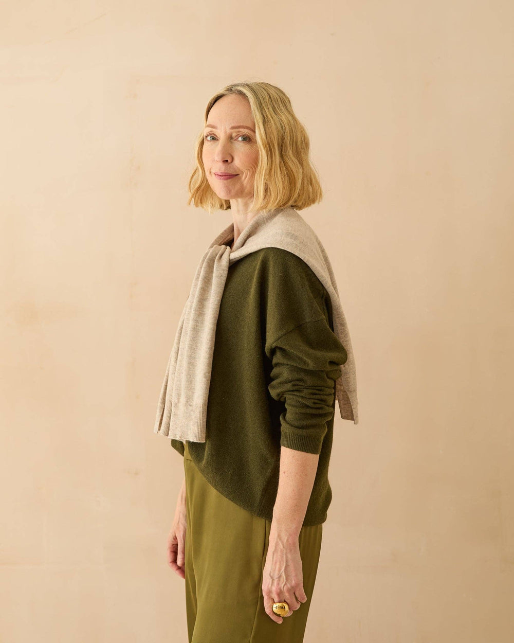 Woman wearing a green outfit with a beige scarf against a beige background