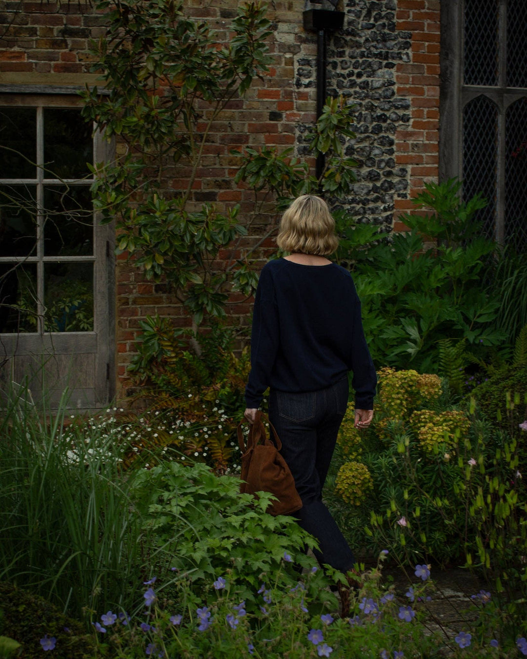 Person walking through a garden with a brick building in the background