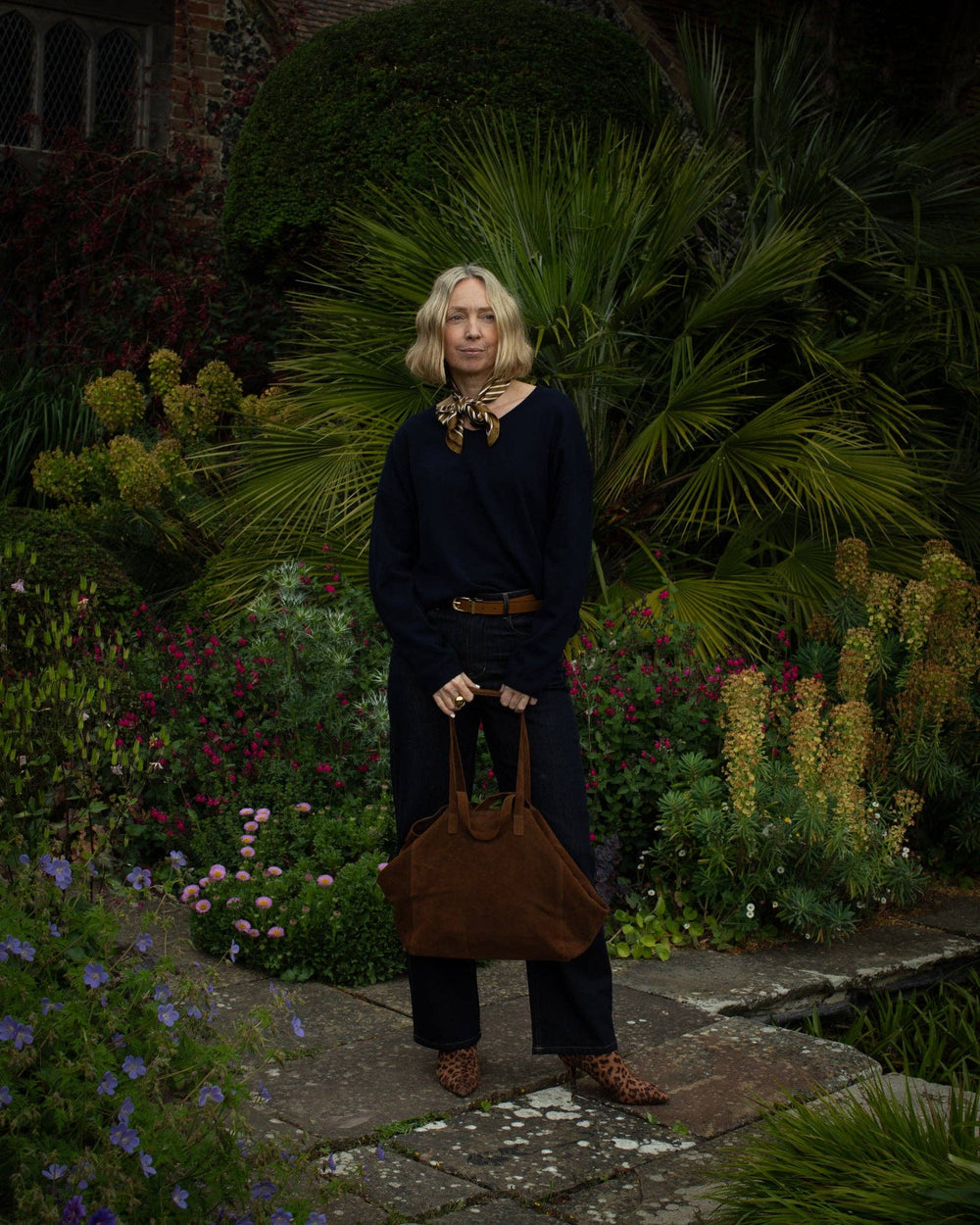 Woman standing in a garden holding a brown leather bag
