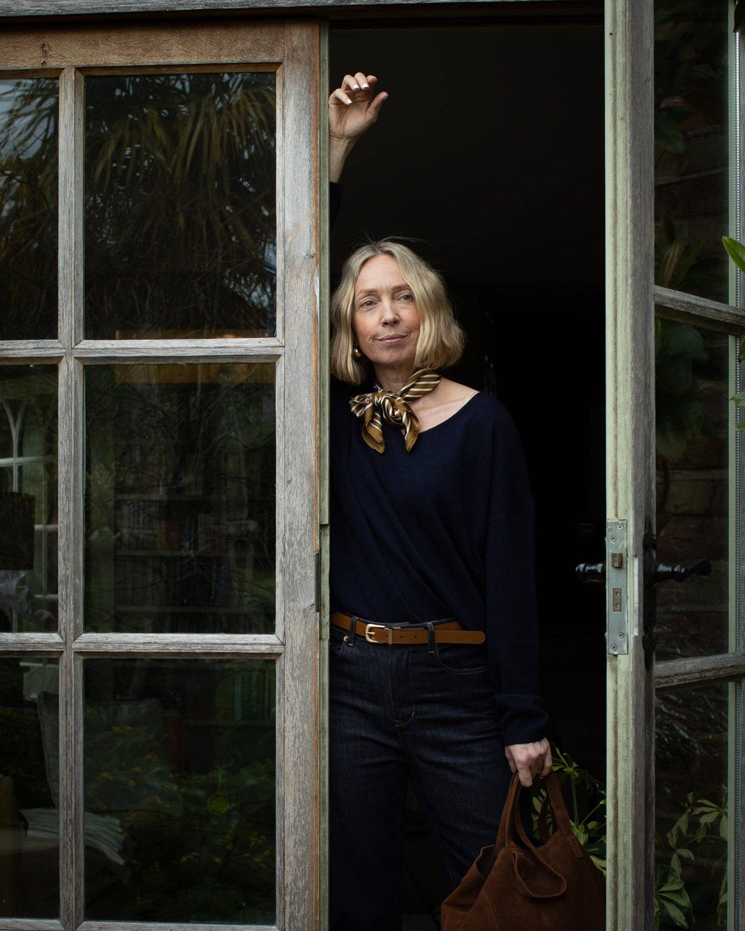 Woman standing by a door with a window, holding a brown bag.
