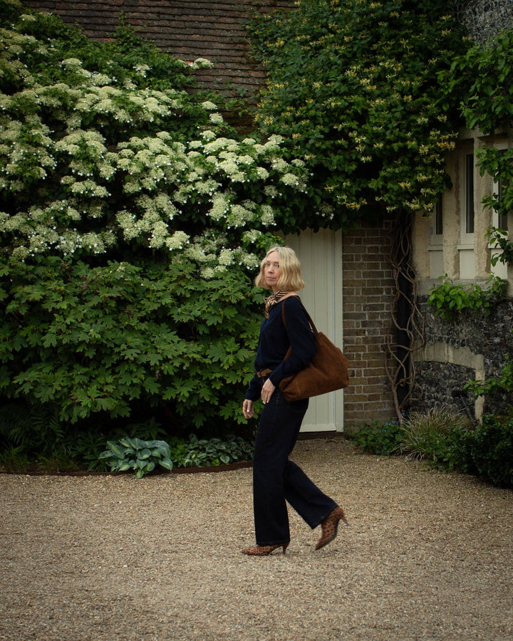 Woman walking in a garden with greenery and a building in the background