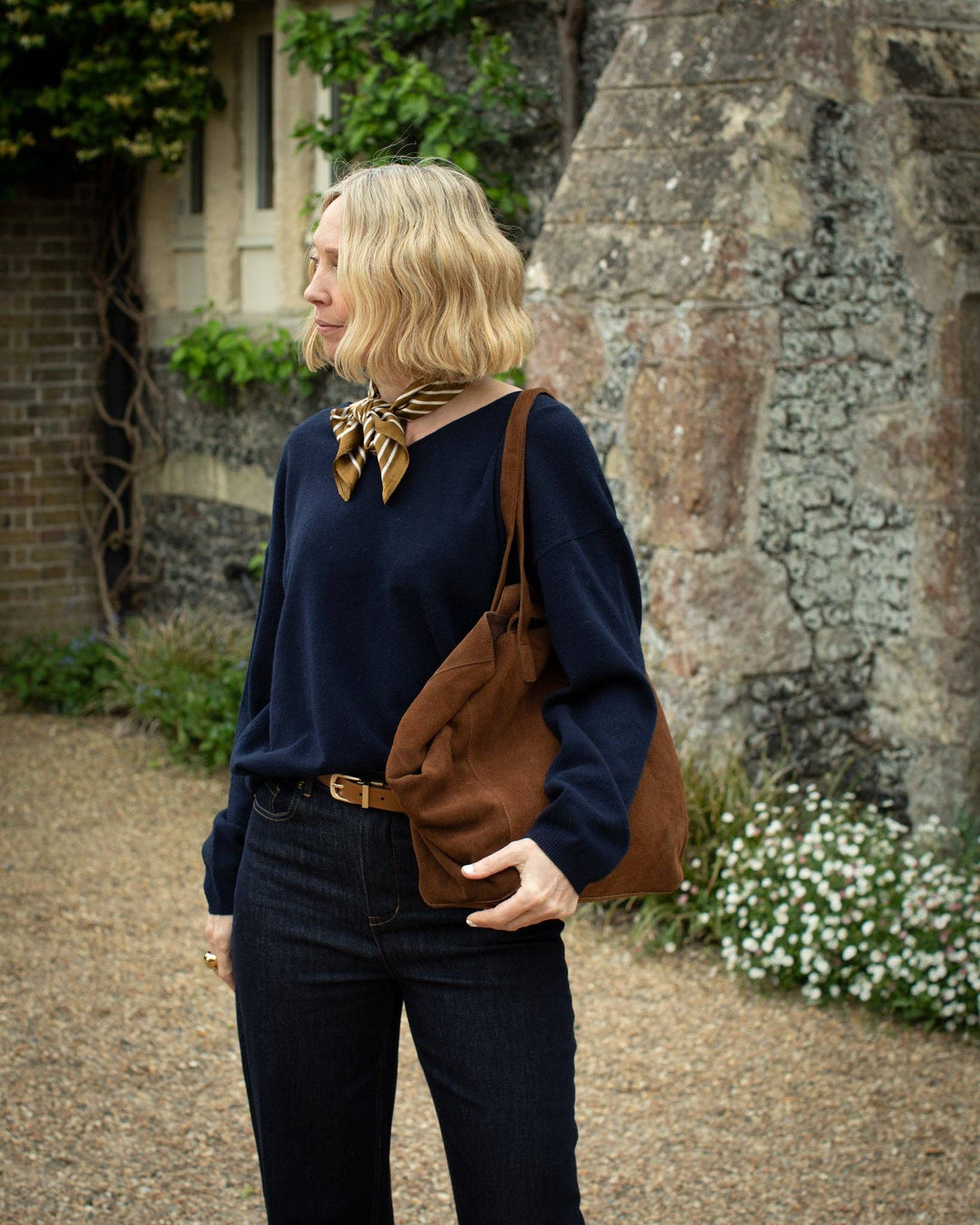 Woman with a brown bag standing outdoors near a stone building.