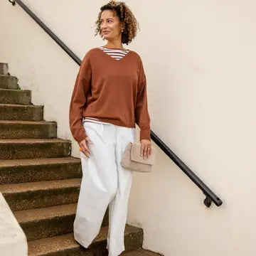 Woman in brown sweater and white pants standing on a staircase