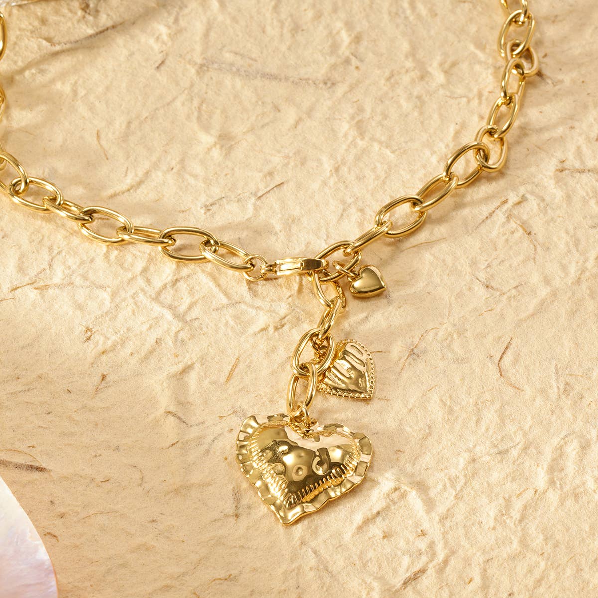 Gold chain necklace with heart-shaped pendants on a beige textured background