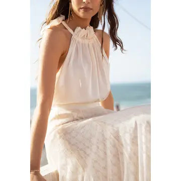 Woman wearing a white dress sitting by the ocean.