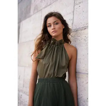 Woman wearing an olive green halter top and skirt against a stone wall.