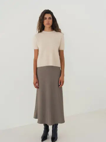 A woman modeling a two-tone knit sweater and midi skirt set. The top is a short-sleeve cream knit, and the skirt is a solid taupe-brown.